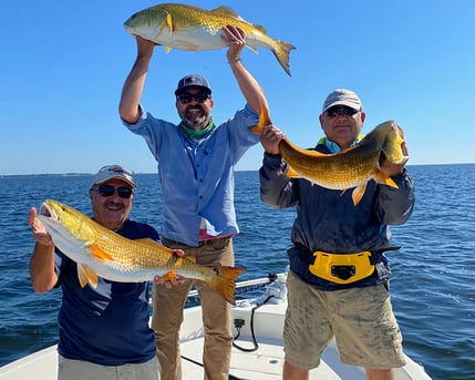 three men holding up redfish on the boat